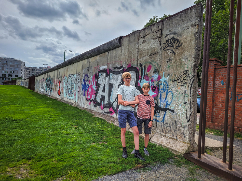 Onze jongens voor een fragment van de Berlijnse muur, waar je ook doorheen kunt via metalen constructies in de openingen.